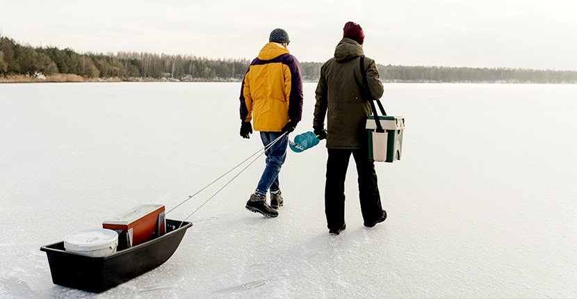 Two people walking across ice with fishing gear
