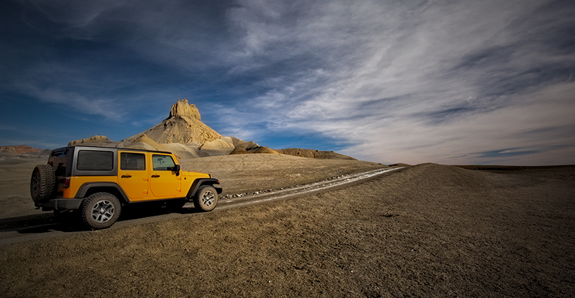 Yellow jeep driving down a desert road