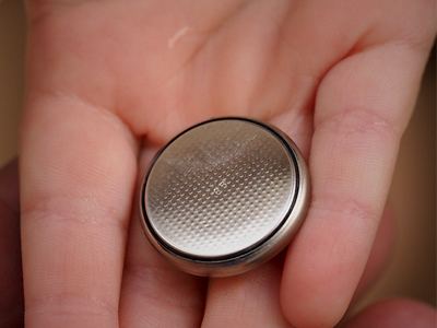 A hand holding a coin cell battery