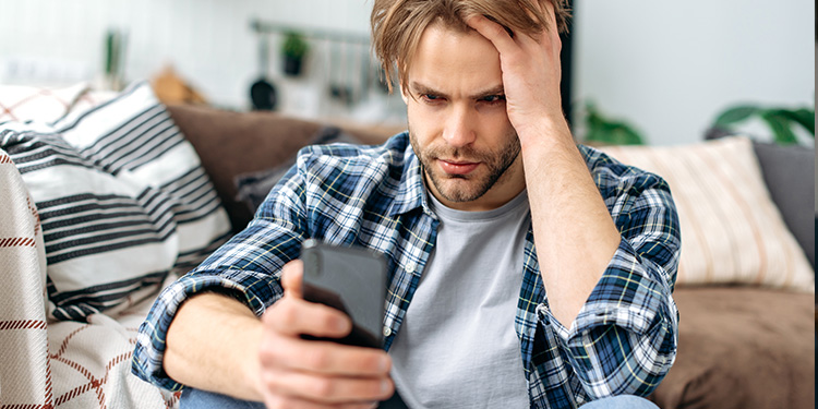 Man sitting on the floor in front of a couch looking stressed at his cell phone