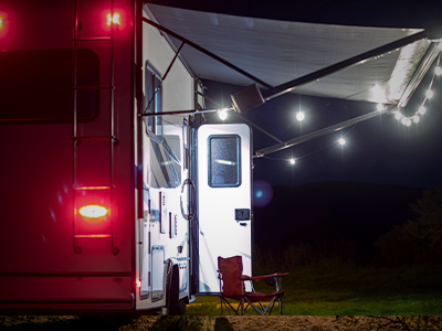 Lit up side of an RV with the door open, awning out and chair