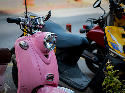 A pink, yellow and red scooter or moped parked in a row