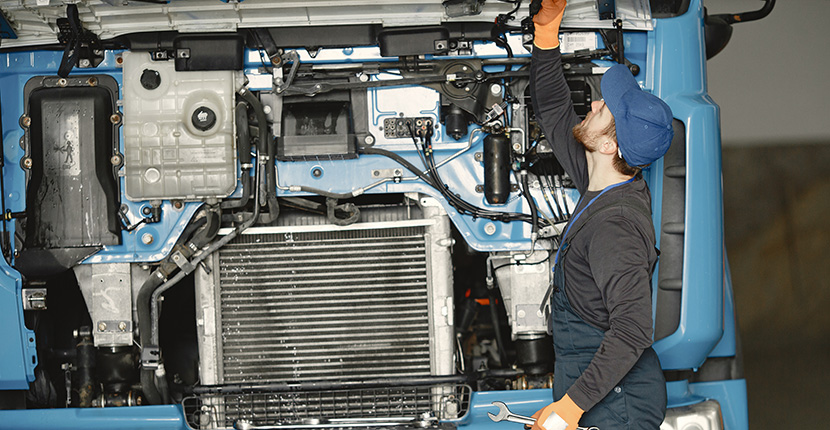 Worker looking at a wire under the hood of a large truck