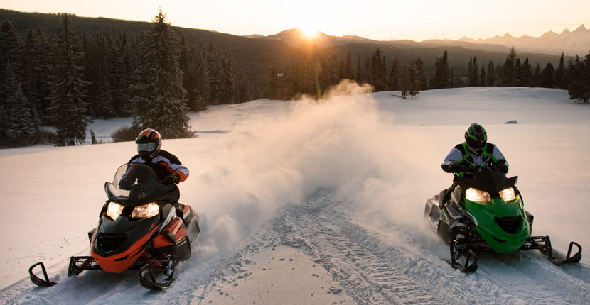 2 people riding snowmobiles in an open area
