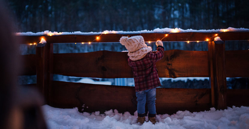 Little girl looking at lights wrapped around a fence